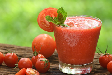 Blended tomato juice with slice tomatoes in glass on nature background