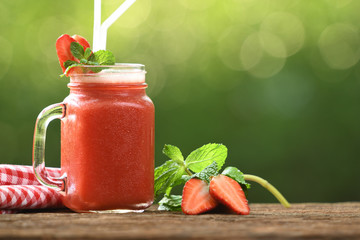  Strawberry smoothie in glass with sliced berries on wood and nature background