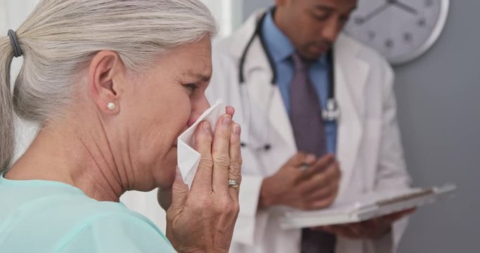 Closeup of sick elderly woman sneezing into paper tissue. Tight view of ill senior patient visiting doctors office blowing nose into tissue
