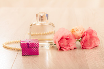 Obraz na płótnie Canvas Bottle of woman perfume with gift box, beads and flowers on pink background
