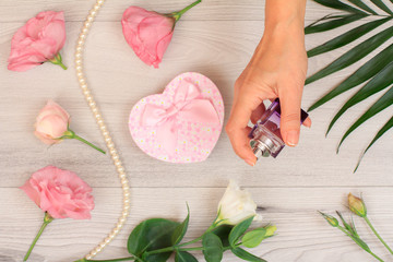 Woman holding a bottle of perfume in the hand with flowers on the background