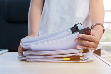 Business Documents concept : Employee woman hands working in Stacks paper files for searching and checking unfinished document achieves on folders papers at busy work desk office. Soft focus