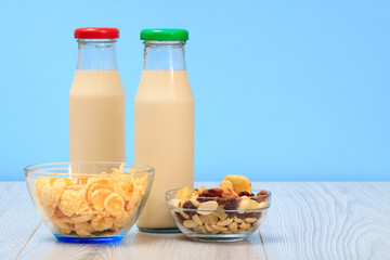 Two bottles of milk with red and green cap and bowls with muesli and cornflakes.