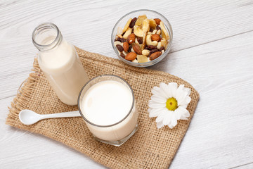 Bottle and glass of milk, bowl with muesli and daisy flower on gray background