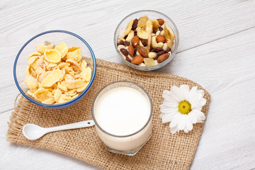 Glass of milk, bowls with muesli and cornflakes on gray background