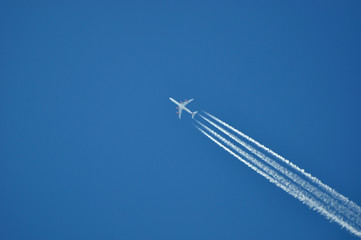 Plane flying with trail in blue sky.
