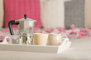 Breakfast in bed. On a white wicker tray there is a coffee maker, coffee cups and croissants.