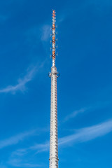 Transmission tower for the transmission of television, radio and mobile in front of a bright blue sky.