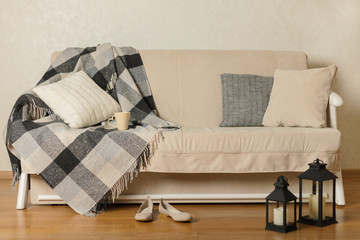 Autumn (winter) concept - coziness and warmth in the house. Beige sofa with plaid and pillows in the living room.