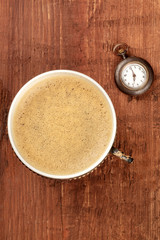 Coffee Time. An overhead photo of coffee in a retro cup, shot from above on a dark rustic wooden background with an old vintage watch showing seven o'clock and copy space