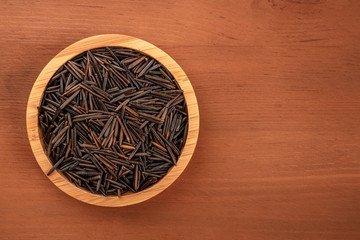 Black wild rice, shot from the top in a wooden bowl on a dark rustic background with copy space