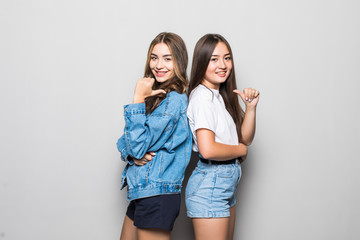 Two pensive young girls dressed in summer clothes standing back to back and pointed each other isolated over gray background