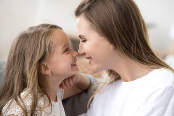 Obraz na płótnie Canvas Smiling cute kid preschool girl and young mother touching noses expressing tenderness and care, loving mom and happy child daughter having fun cuddling together, family sincere relations concept