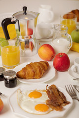 Breakfast time. Fried eggs and bacon. Croissants and orange juice, jam. Coffee with cream or milk. Fruits - bananas, red and green apples.