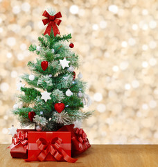 Under the decorated Christmas tree are red boxes with gifts. Tree on the background of lights in blur