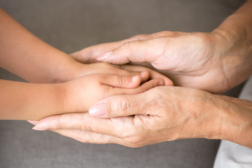 Close up view of senior grandmother holding hands of little kid granddaughter as concept of elderly granny protecting child, different old and baby generations, giving love care support to grandchild
