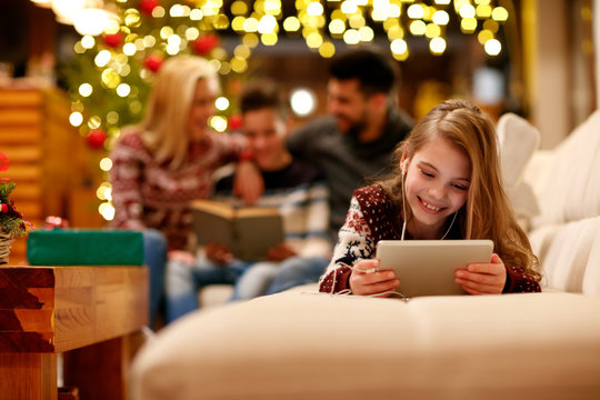 little girl with headphones is using a tablet and smiling on Christmas day.