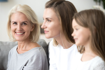 Portrait of smiling mature grandmother looking at camera near young daughter and kid granddaughter looking forward to good future, three 3 women family, older elderly generation getting old concept
