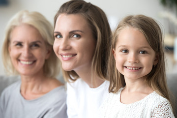 Smiling cute kid girl daughter looking at camera with young mother and old grandmother, happy little child posing for portrait with mom grandma, growing up in multi-generation 3 women family concept