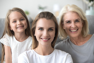Smiling young adult woman looking at camera with old mother and little kid daughter, millennial mom...