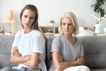 Upset older mother in law and adult daughter sit back to back not talking after fight disagreement, two stubborn old young women ignoring avoiding each other sad by argument, family conflict concept - obrazy, fototapety, plakaty