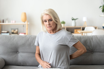 Worried sad mature older woman touching back feeling ache massaging tensed muscles, upset senior...