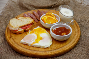 Natural homemade breakfast of scrambled eggs, toast, hunting sausages and jam, laid out on a wooden plate. The concept of healthy and tasty breakfast.