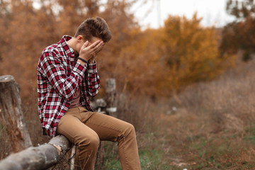 sad young man sitting on wooden fence