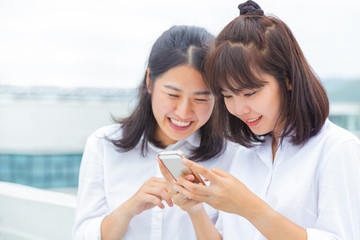 Two young woman enjoy using their smart phone to connect to digital social media