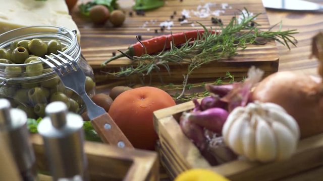 Olive oil, salt, pepper, seasoning herbs and fresh vegetables tomato, onion, garlic for cooking tracking  shot. Close up vegetables and seasoning background on kitchen.