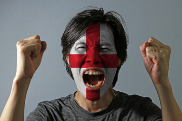 Cheerful portrait of a man with the flag of the England painted on his face on grey background. The concept of sport or nationalism. red centred cross on a white background. - Powered by Adobe