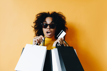 Black friday. Shopping. Afro American girl in sun glasses is holding shopping bags and a credit...
