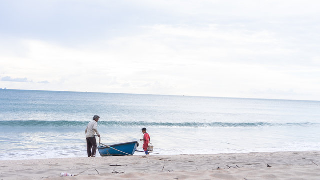 Grandfather And Grandson Pulling A Row Boat Into The Sea To Go Fishing