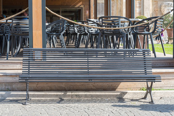 Wooden bench in the city Park and plastic chairs in the background.