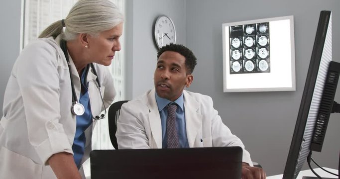 Close up of two doctors looking at computer monitor comparing notes. Young black doctor typing on laptop computer while consulting with white senior colleague