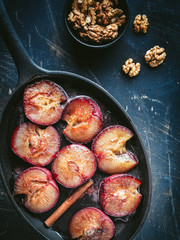 Roasted red greengages on baking pan and walnuts in black bowl. Overhead view. Dark and moody.