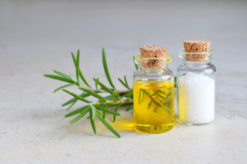 Rosemary essential oil in a small bottle and fresh twig on light background. Natural aroma cosmetic oil and salt