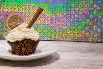 Holiday muffin with mascarpone frosting, dried orange, lemon and lime slices decoration, cimmanon rolls and anise stars. Bright colorful background.