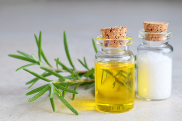 Rosemary essential oil in a small bottle and fresh twig on light background. Natural aroma cosmetic oil and salt