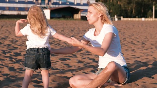 Beautiful blonde mom and daughter cuddling and speaking on the beach at sunset.