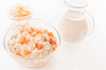 Oatmeal with pumpkin and nuts in a glass plate and a jug with milk on a white background. Close-up. Copy space