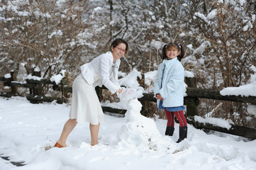 Fototapeta na wymiar Young and beautiful mother with her daughter smiling and playing with snow next to a fence of tree trunk. Shizuoka Prefecture, Japan. Winter of February 2011.