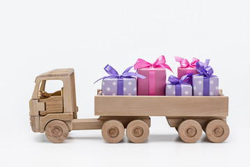 Boxes with gifts in purple with white polka dots and pink paper, carrying  toy wooden truck. Holiday concept.