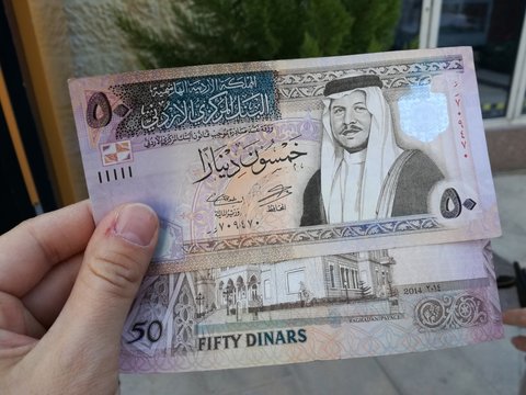 Male hand holding Jordanian dinars banknotes in front of a window.