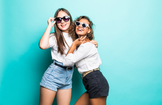 Friends Forever. Two Mixed Race Cute Lovely Girl Friends In Sunglasses Posing With Smile On Blue Background