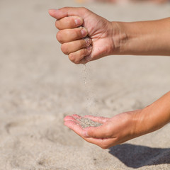 The girl pours sand from one hand to another. Closeup. Young woman with sand in her hands.