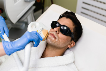 Young good looking man getting hair removal cosmetology procedure at cosmetic beauty spa clinic.