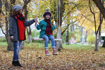 Young beautiful mother with her daughter on nature. A girl in a hat walks in the park. Girl in autumn city park in leaf fall.