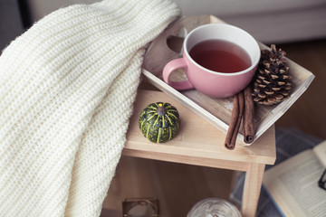 Knitted, warm sweaters, a cup of hot tea, autumn decor, a book, a pumpkin on a wooden chair. Cozy, autumn decor. Autumn interior, sofa. Autumn. Winter.