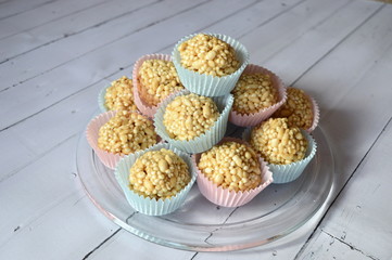 Closeup homemade cones made of puffed cereals, mainly rice and millet groats with fudge candy in colorful cupcake wrappers with blurred background